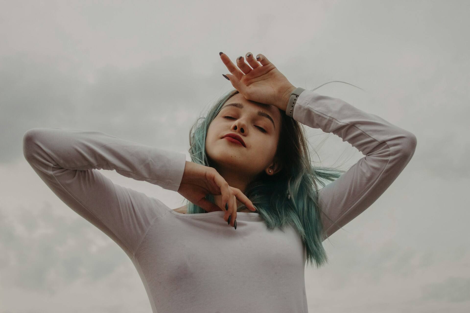 A woman with closed eyes and raised arms, expressing embodied emotional awareness against a neutral background.